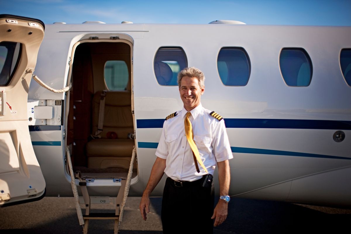 A pilot standing in front of a private jet and smiling